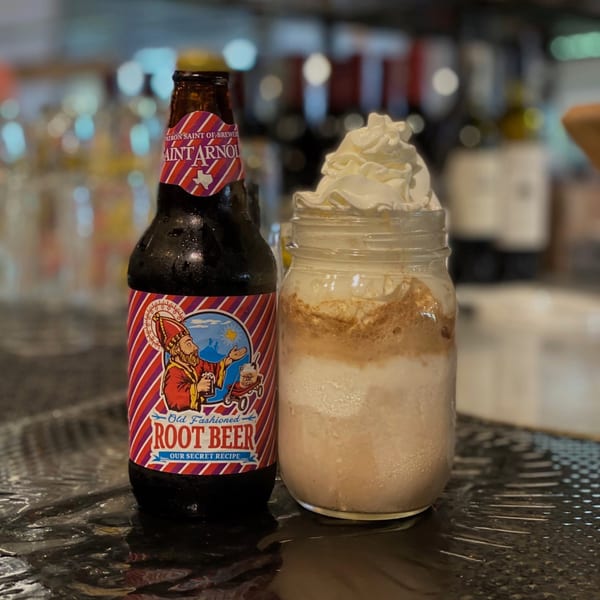 A bottle of Saint Arnold Root Beer next to a root beer float with whipped cream in a mason jar.