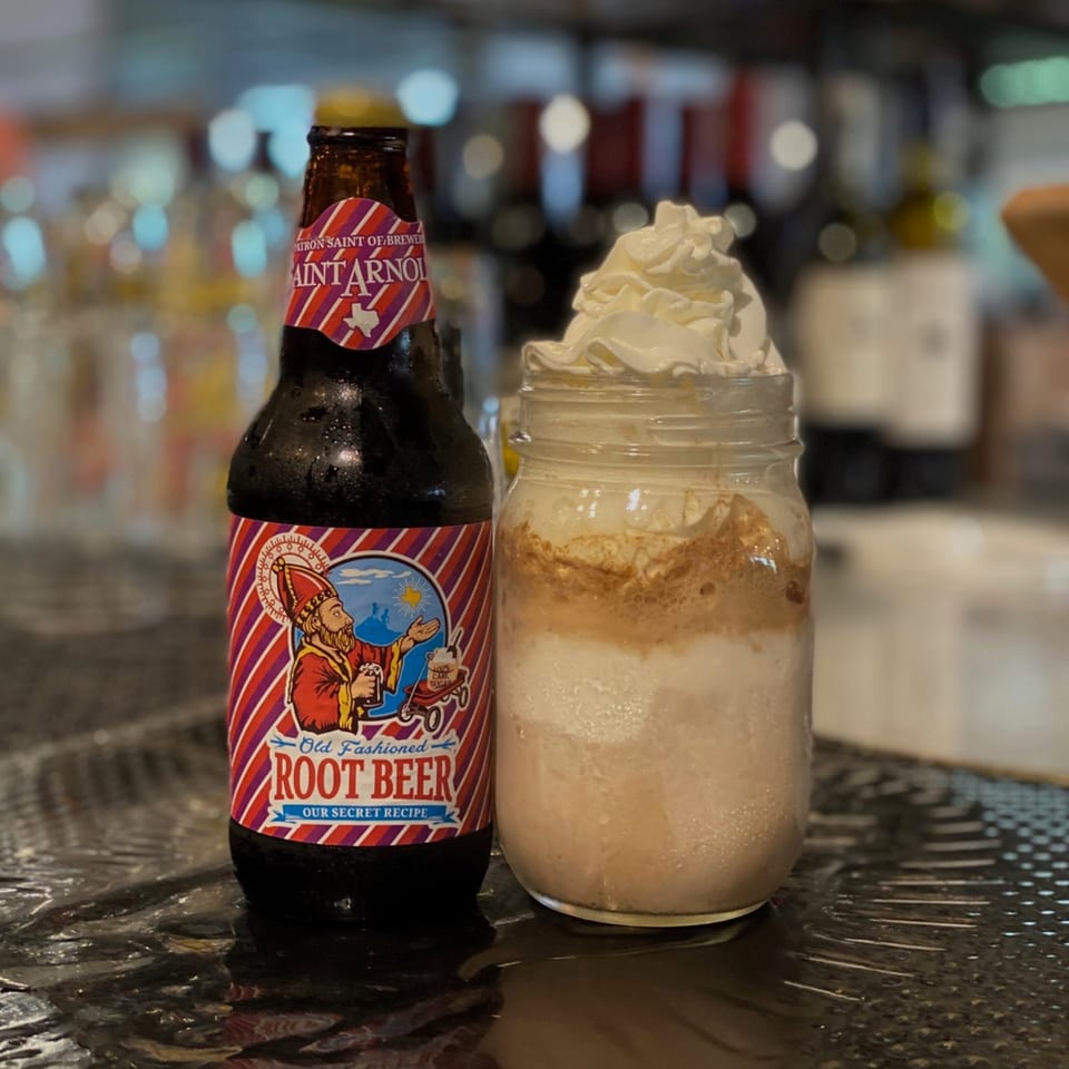 A bottle of Saint Arnold Root Beer next to a root beer float with whipped cream in a mason jar.