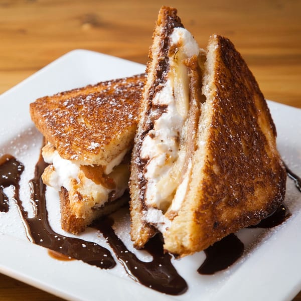 Two halves of a dessert grilled cheese sandwich with marshmallow, chocolate, and powdered sugar.