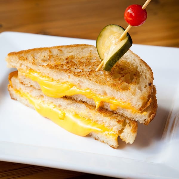 Grilled cheese sandwich halves on a white plate, garnished with a pickle and cherry.