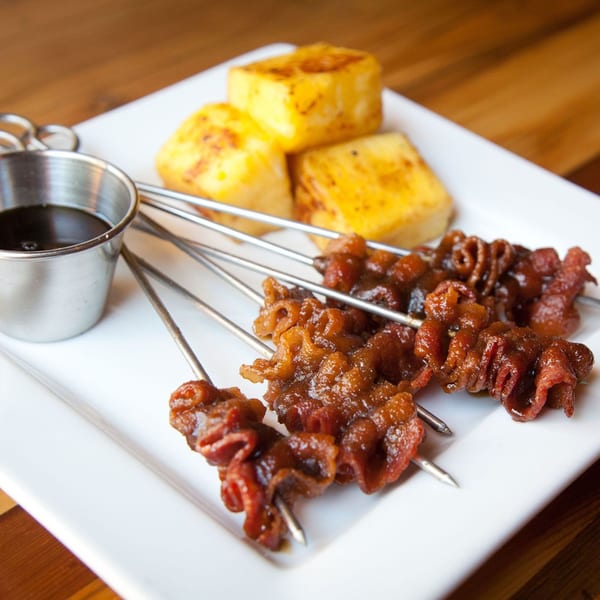 Bacon skewers with a side of golden-brown grilled cheese cubes and a dipping sauce.