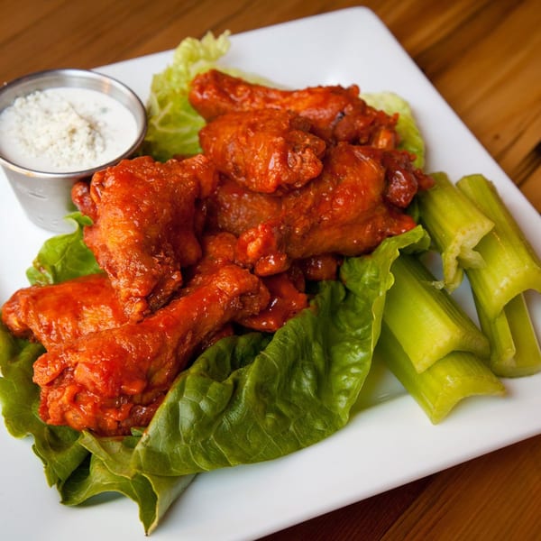 Spicy Dallas Grilled Cheese Co. buffalo wings with blue cheese dressing, lettuce, and celery sticks.