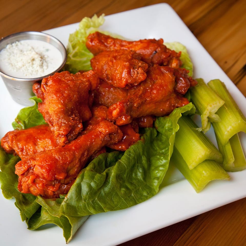 Spicy Dallas Grilled Cheese Co. buffalo wings with blue cheese dressing, lettuce, and celery sticks.