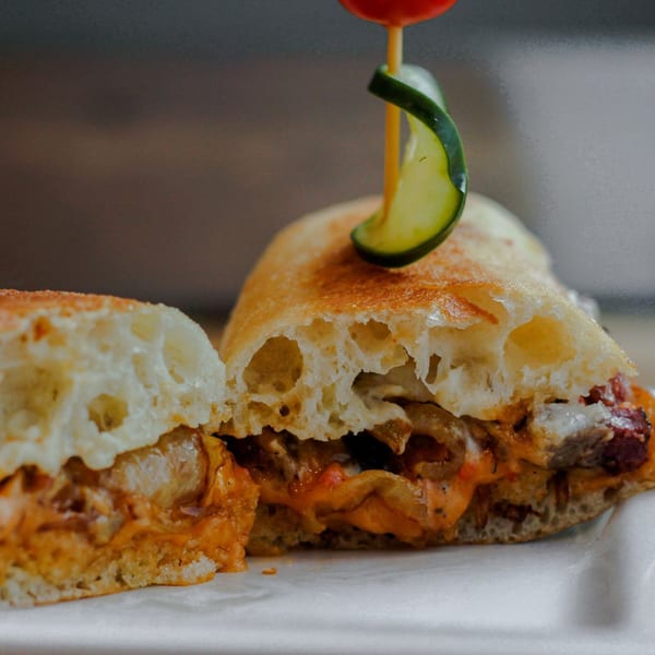 A Dallas Grilled Cheese Co. sandwich, cut in half, revealing melted cheese and fillings, garnished with a cucumber slice.
