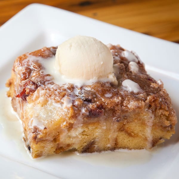 Bread pudding with vanilla ice cream and a sweet glaze on a white plate.