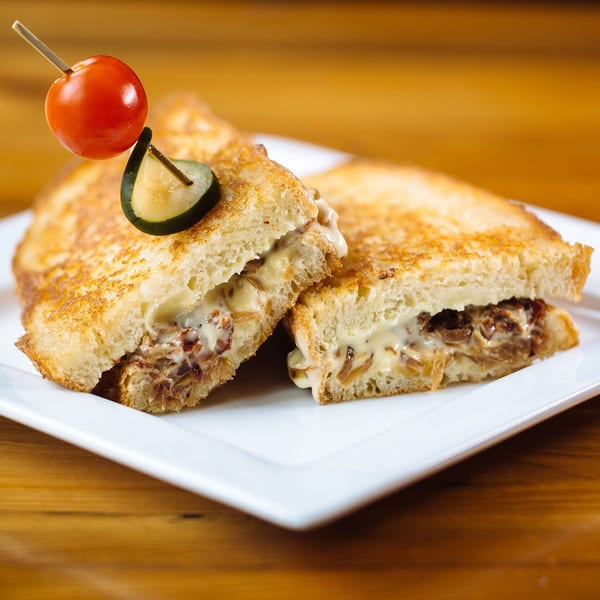 Grilled cheese sandwich halves with caramelized onions and melted cheese, garnished with a cherry tomato and olive.