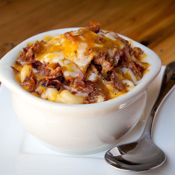 A white bowl of creamy mac and cheese topped with melted cheese and crispy bacon bits.
