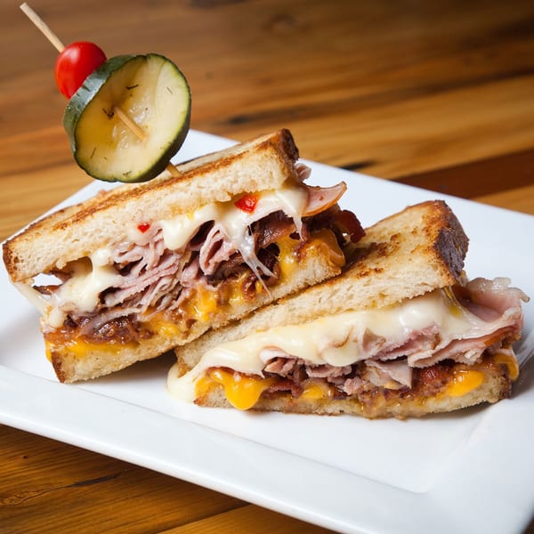 Dallas Grilled Cheese Co. sandwich with melted cheese, meat, caramelized onions, and a pickle spear.